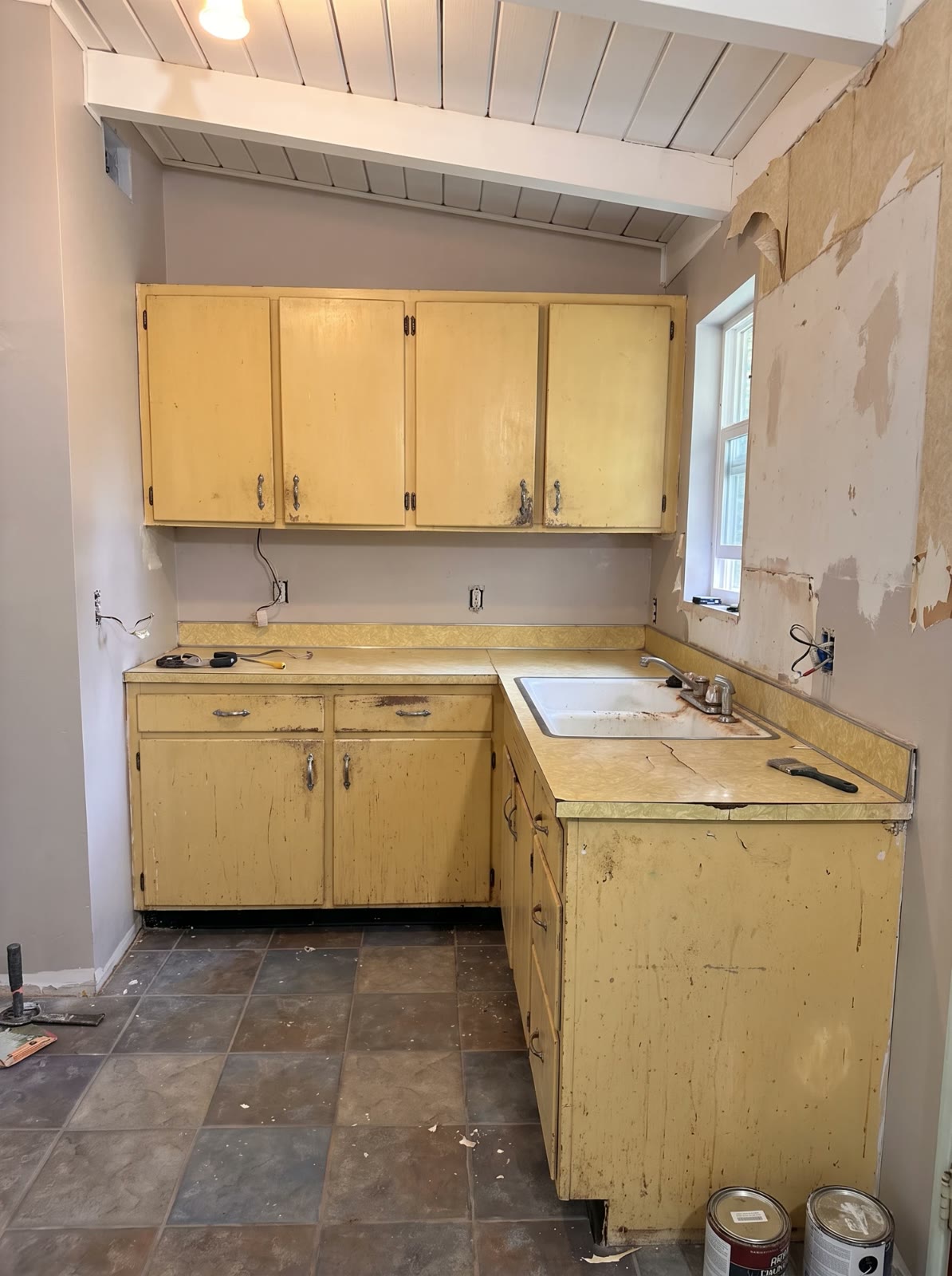 The kitchen before: worn yellow cabinets, a cracked counter and peeling wall covering